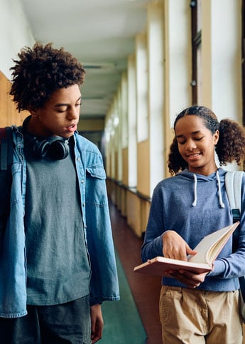 Two students looking at looking at notebook while walking between classes